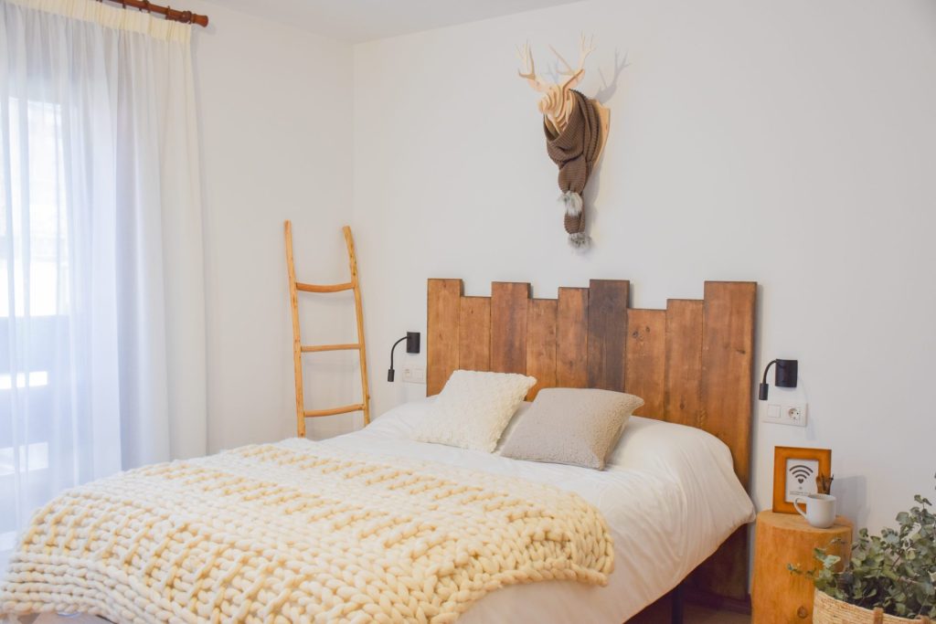 Dormitori de l’apartament ROC al Pas de la Casa: llit de matrimoni amb capçal de fusta, manta de llana i decoració de muntanya