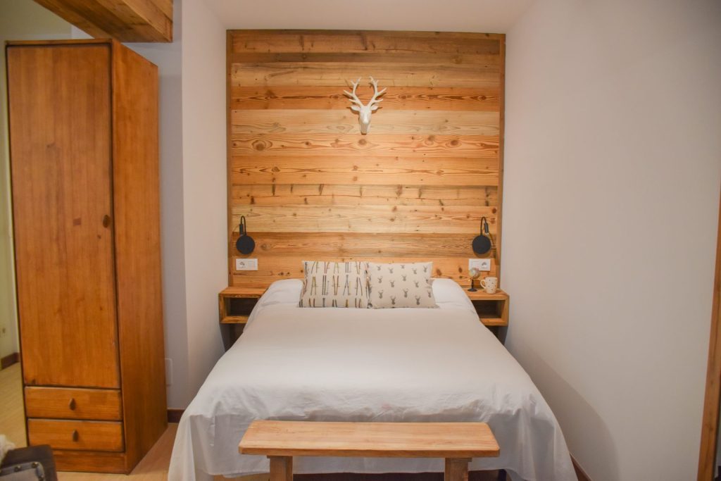 Dormitori de l’apartament WOODY al Pas de la Casa: llit de matrimoni amb paret de fusta natural i armari de fusta